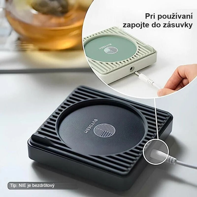 Čierny ohrievač hrnčekov zapojený do zásuvky, vedľa hrnček